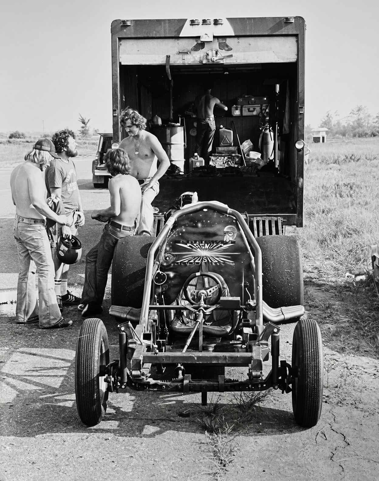 Body-off Magnum Illusion chassis beside its trailer, showing lettering, a starburst and helmeted portrait painted behind the cockpit.
